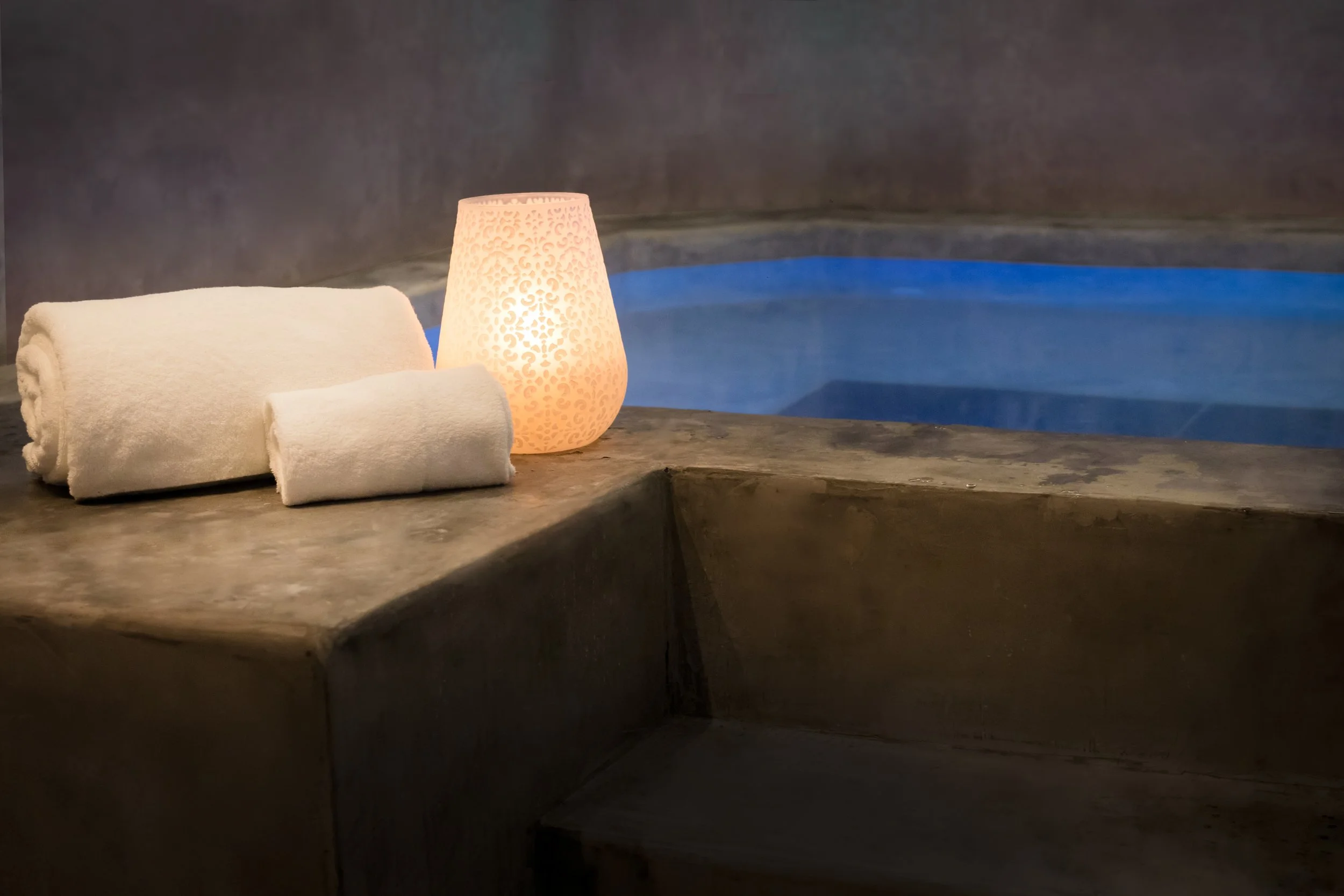 A rolled white towel, a decorative lamp, and a swimming pool in the background.