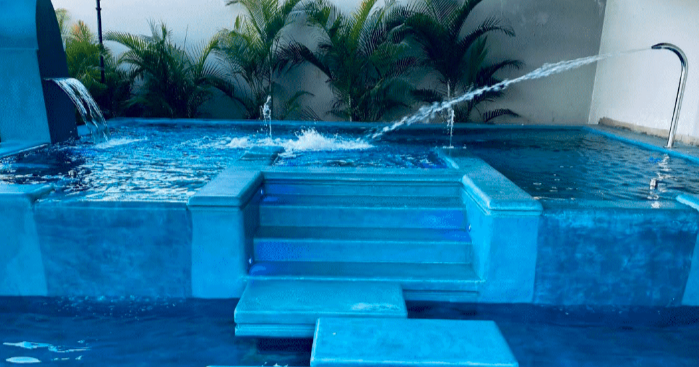 Close-up of a modern, outdoor blue swimming pool with stairs leading into the water, surrounded by green plants.