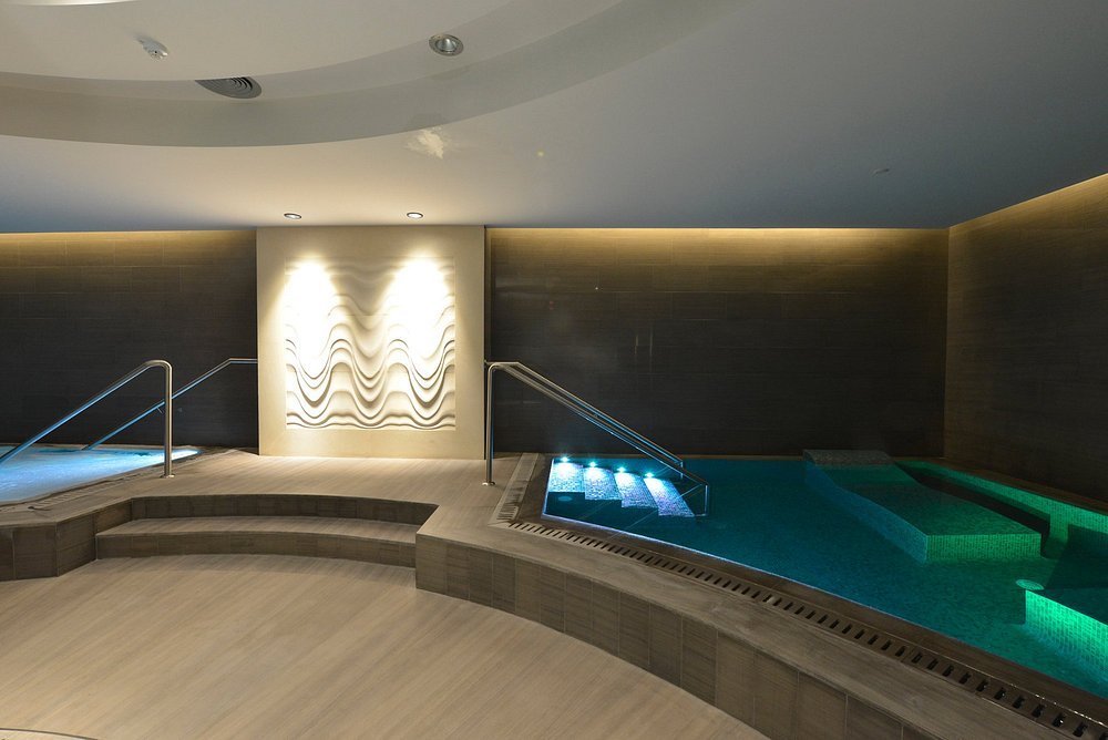 Indoor spa area with a small pool, underwater lighting, steps, handrails, and modern wall decor.