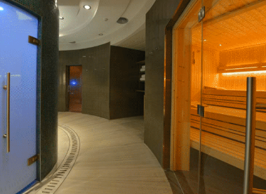 Indoor corridor with wooden sauna on the right, glass door, blue door on left, and curved ceiling.