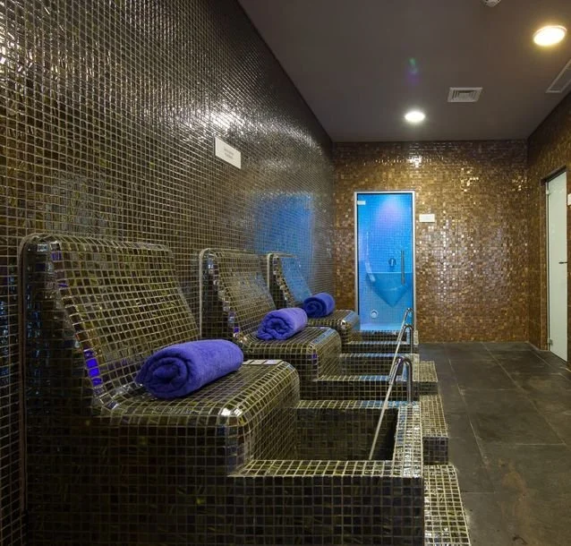 Spa washroom with three tiled foot baths, each with a rolled purple towel, a door at the back leading to a shower, and a doorway on the right.