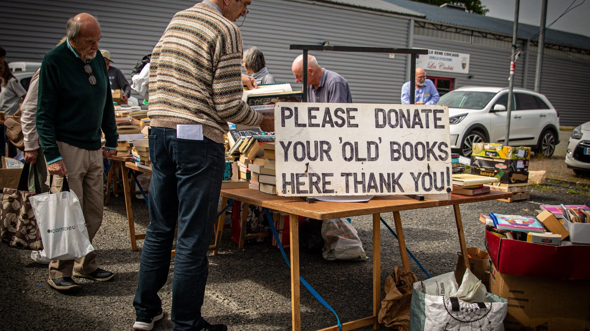 People browsing and donating old books at an outdoor book sale with a sign that says "Please donate your old books here. Thank you!"
