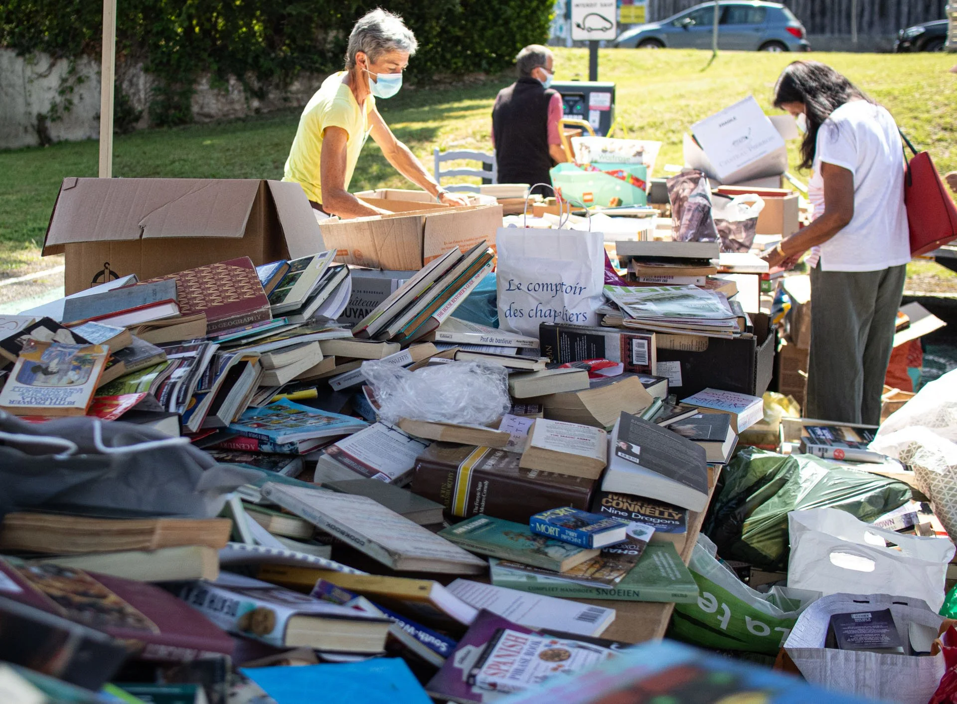 People browsing books at an outdoor book sale or flea market, with tables filled with books and people wearing face masks.