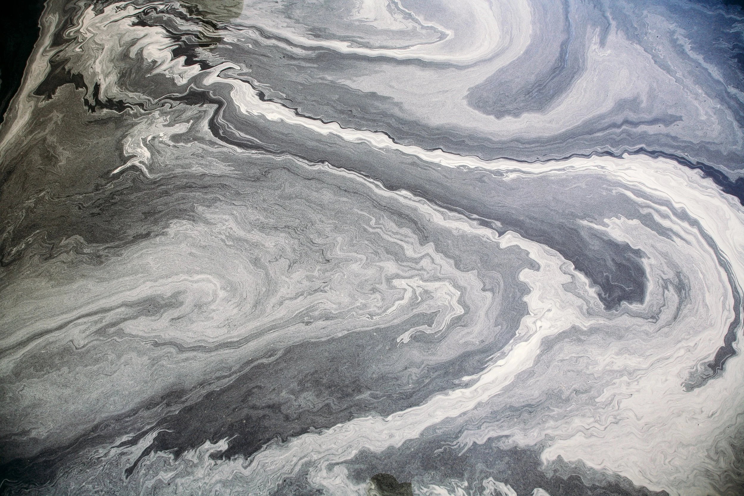 Aerial view of a swirling, layered rock formation with shades of gray, black, and white.