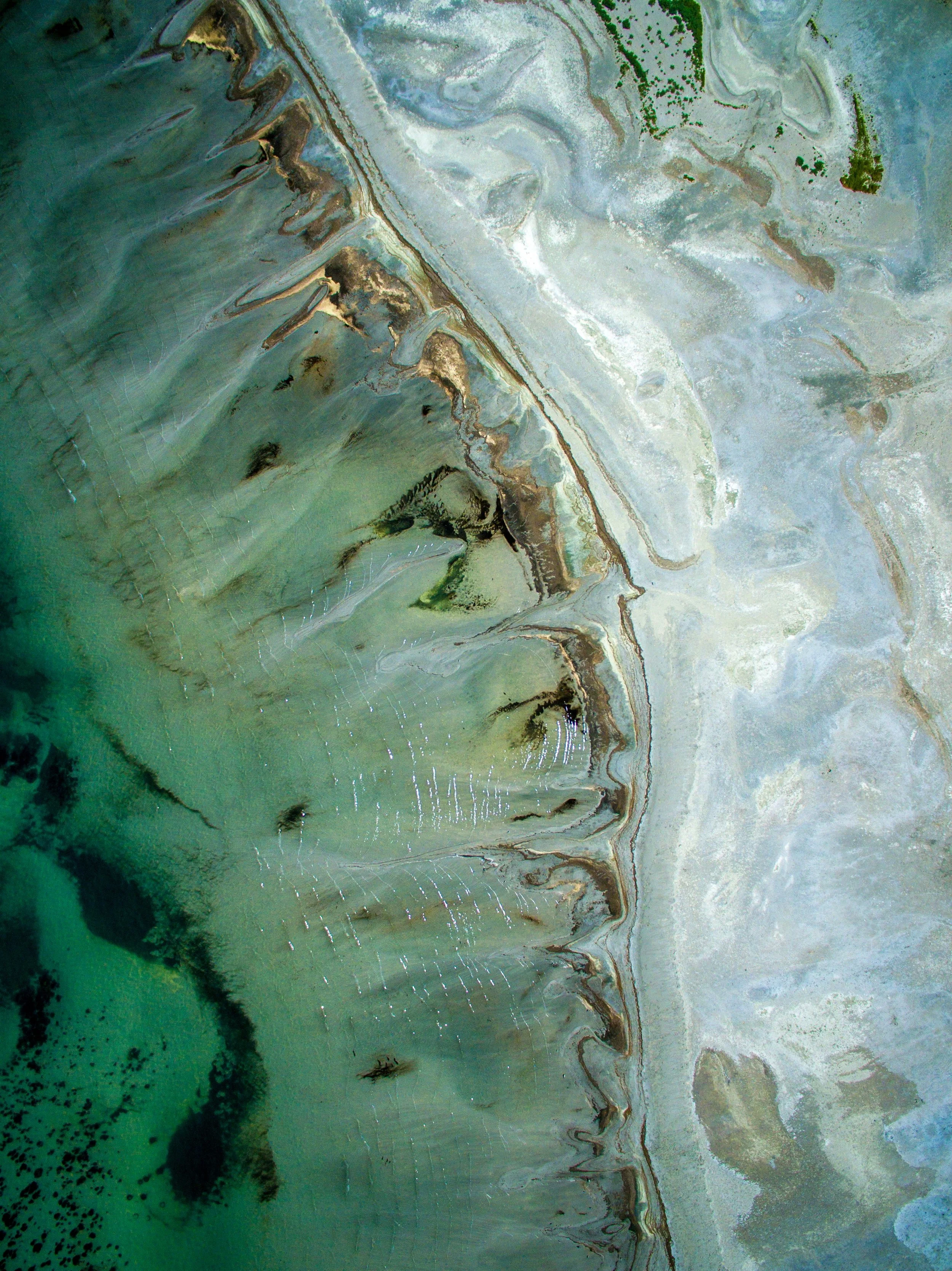 Aerial view of a coastal area with salt flats, salt ponds, and a green landscape with patches of trees.