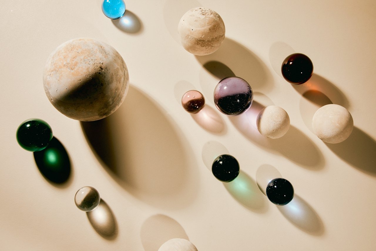 Various sized marbles and textured spheres cast shadows on a white surface.
