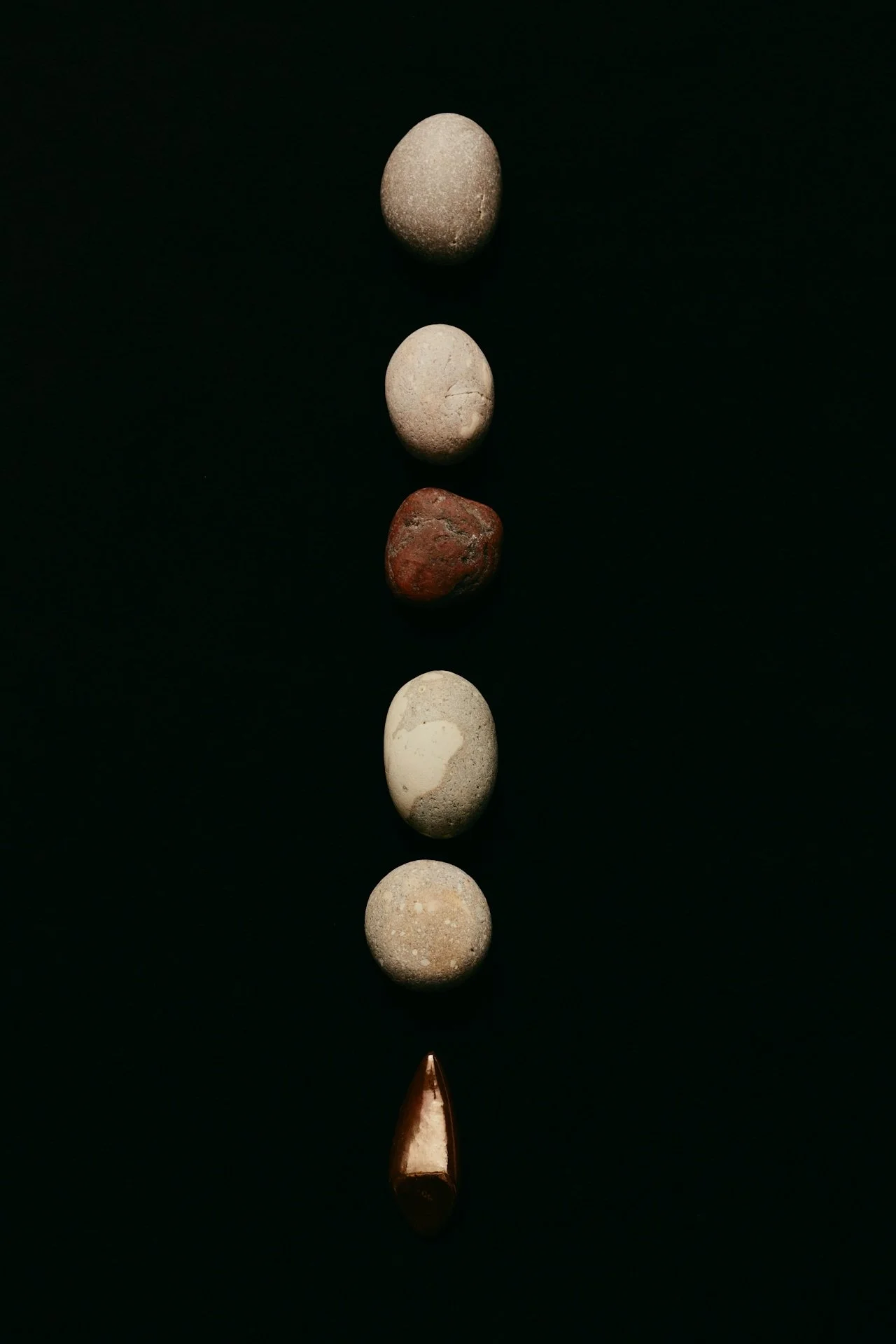 A vertical line of seven different stones against a black background, with a metallic object at the bottom.