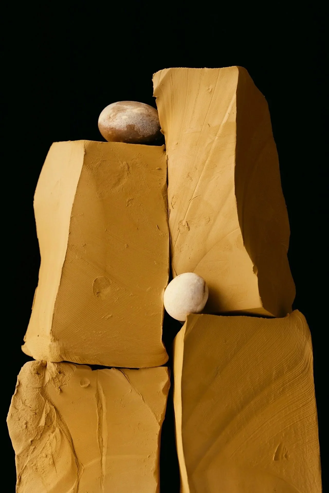 Close-up of beige and yellow clay blocks stacked vertically against a black background with small white stones on top.