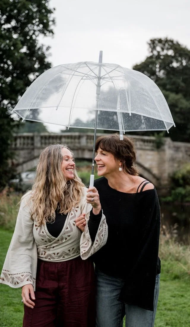 Two women walking beneath an umbrella during a rainy seasonal gathering in Scotland.