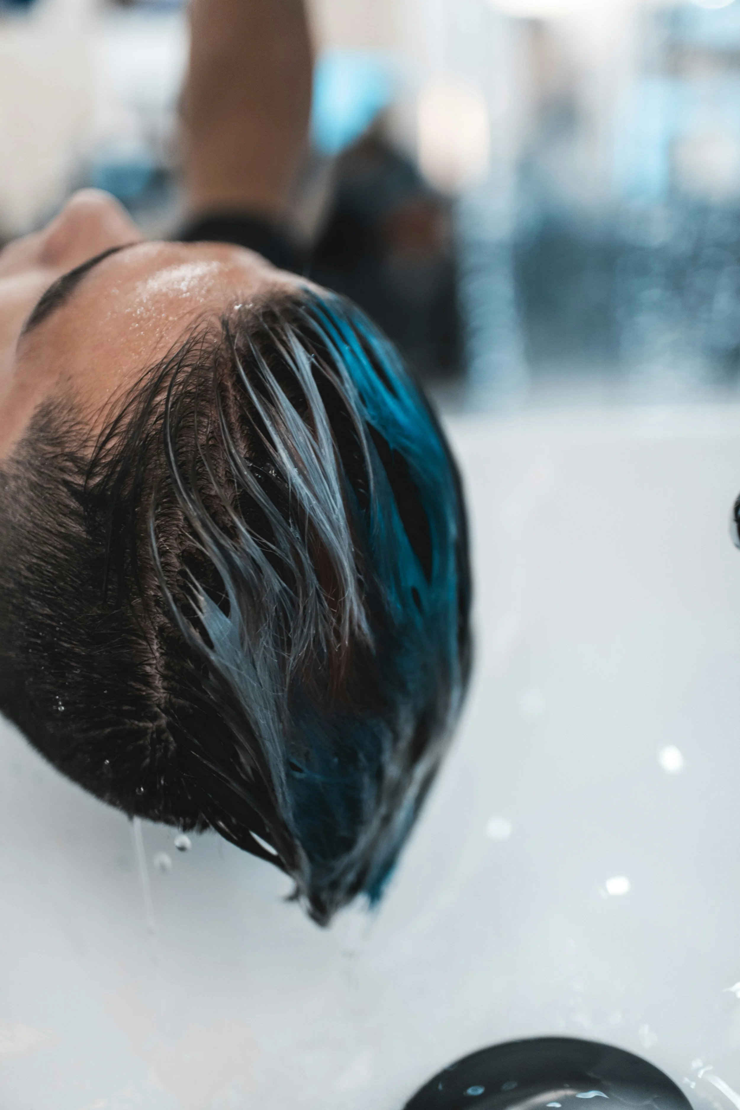 Close-up of a person with wet hair lying on their back, with water dripping from their hair, getting a hair treatment.