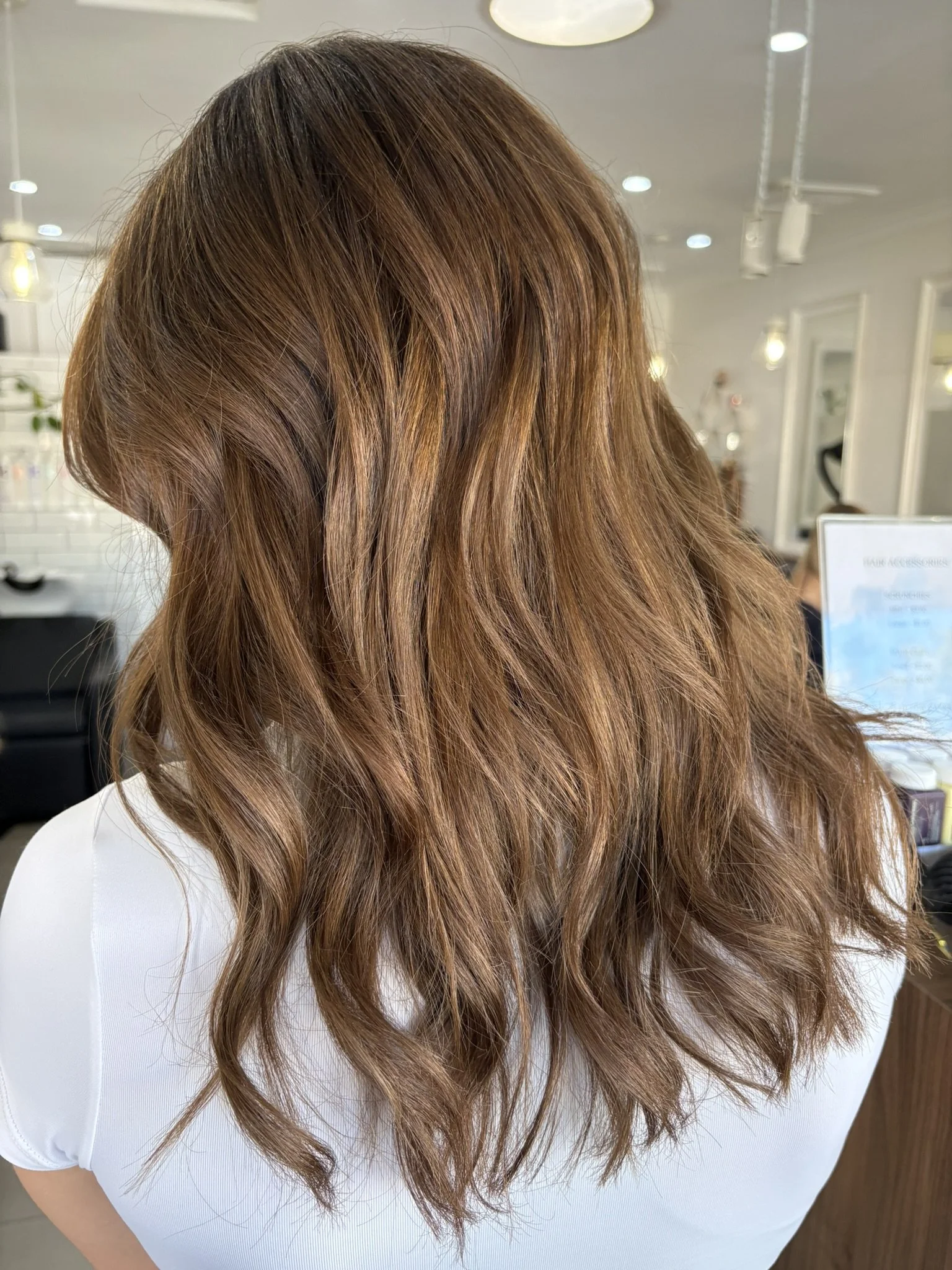 Close-up of a person's long, wavy, reddish-brown hair on a woman wearing a white shirt in a salon.