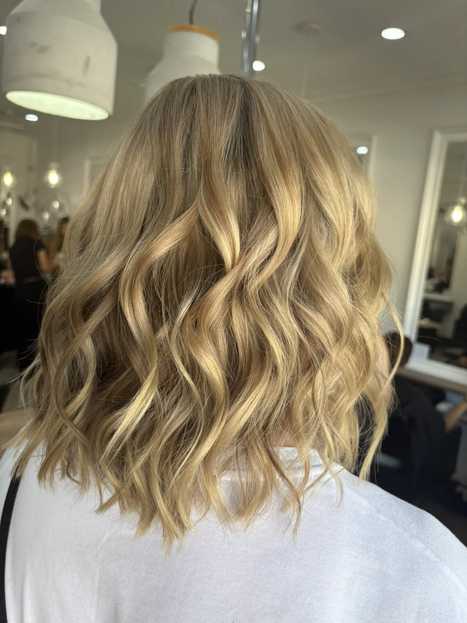 Back of a person's head with long, wavy blonde hair in a salon.