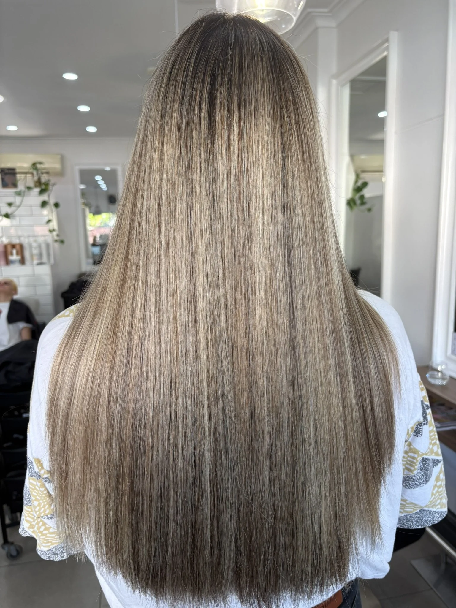 Back view of a person with long, straight, blonde hair in a salon setting.