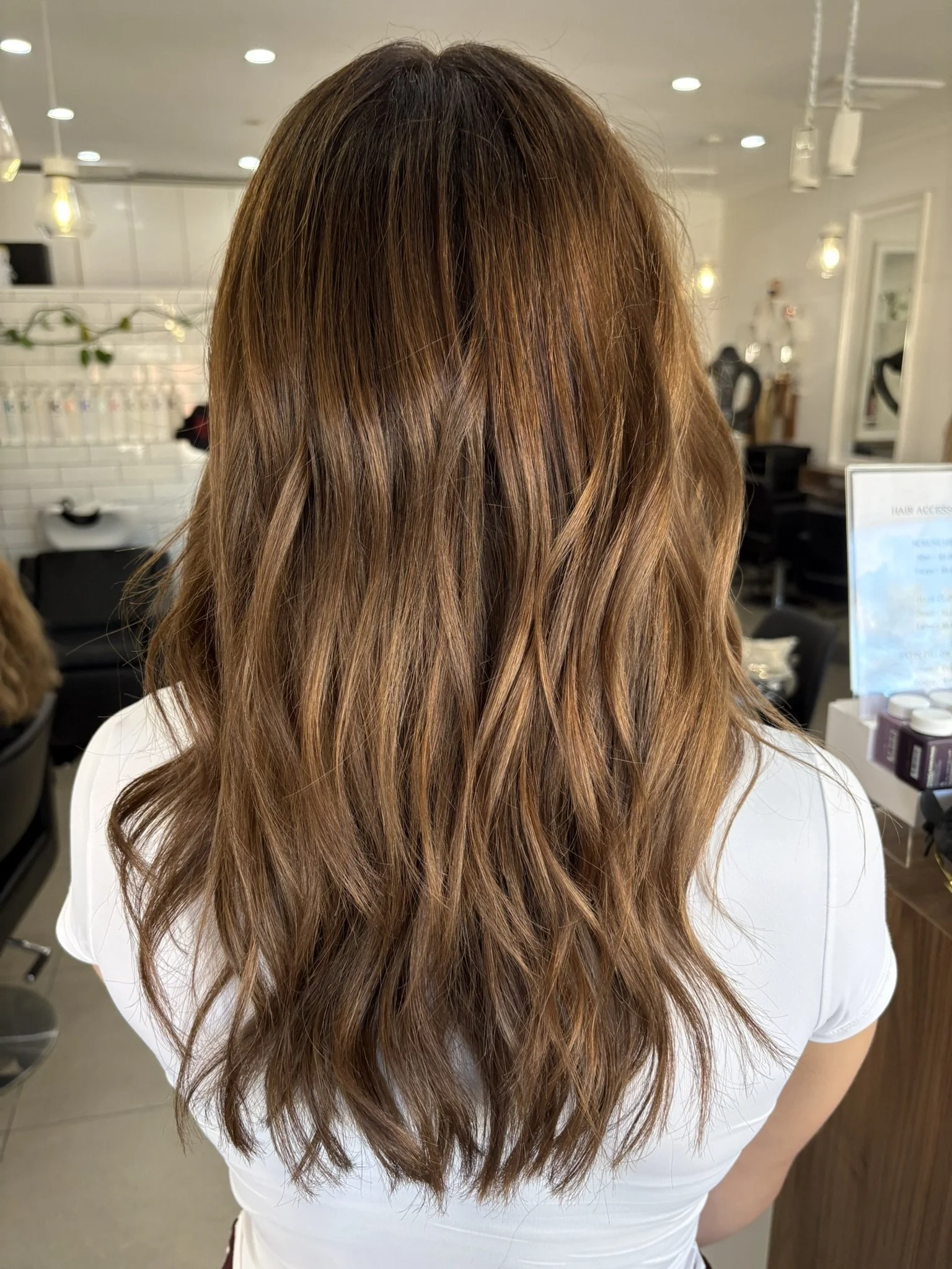 Back view of woman with long, wavy, light brown hair in a salon.
