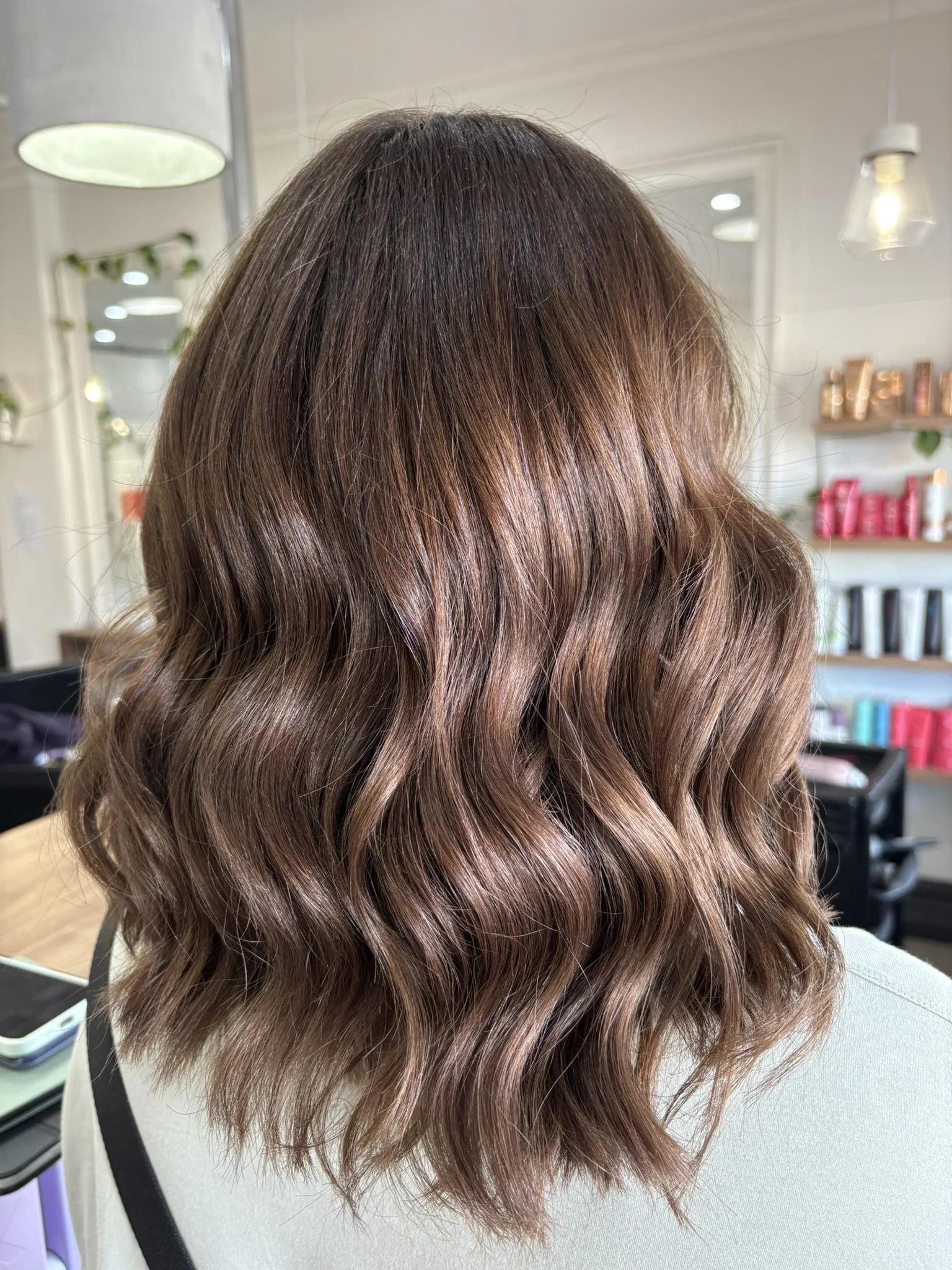 Brown, wavy, shoulder-length hair with subtle highlights, styled in loose curls.