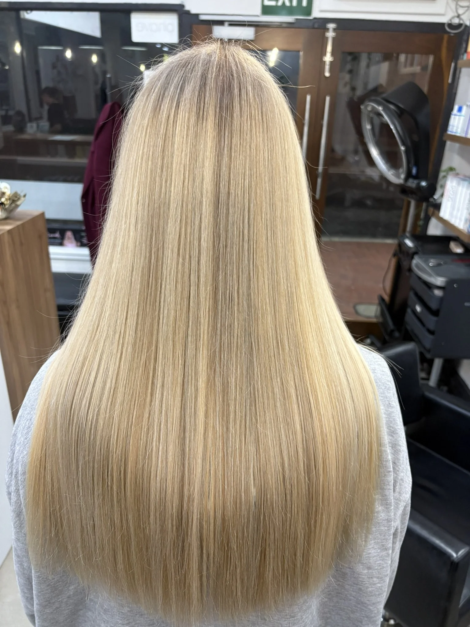 Back view of a person with long, straight, blonde hair in a salon