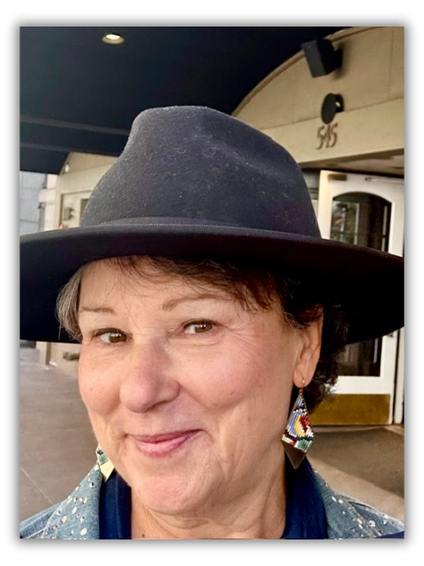 A woman in a black hat and colorful earrings smiles close up
