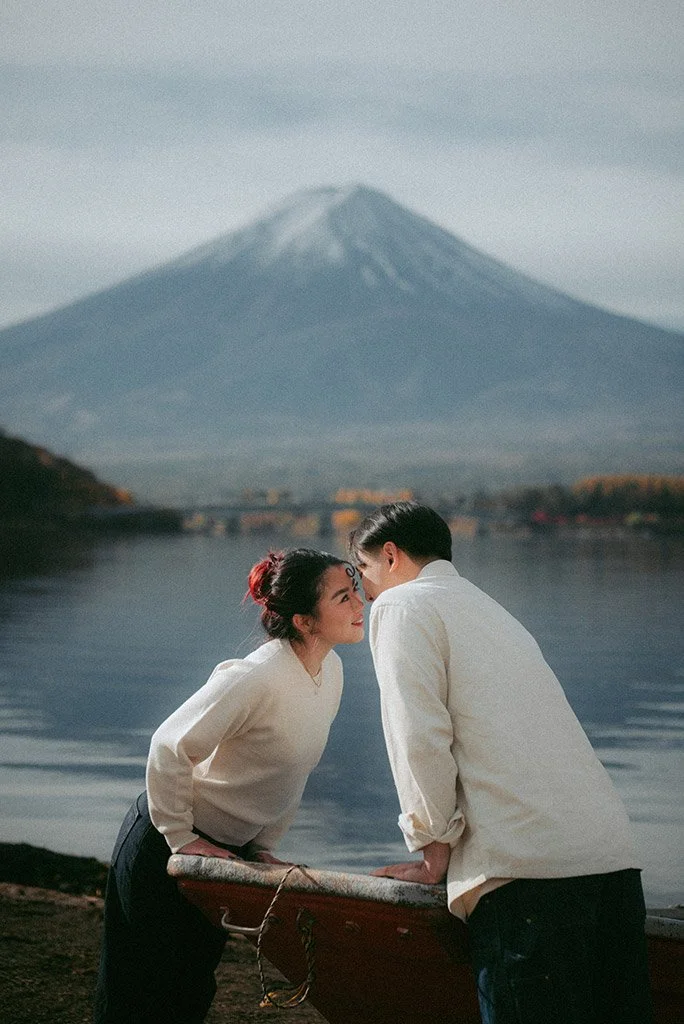 A couple leaning on a boat by a lake with Mount Fuji in the background.