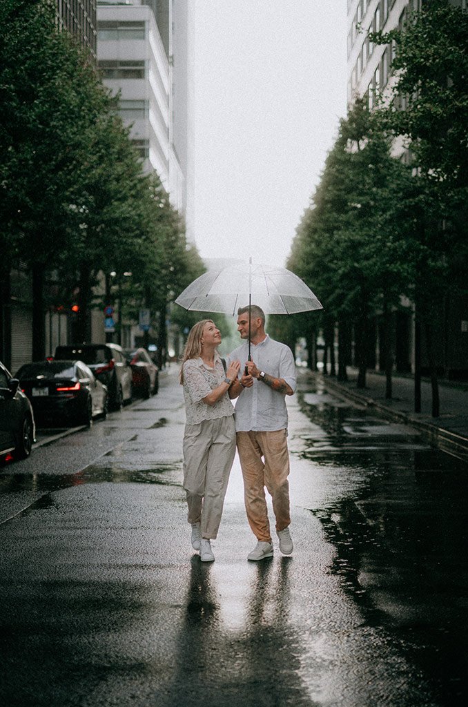A couple walking with an umbrella in a rainy city street, looking at each other.