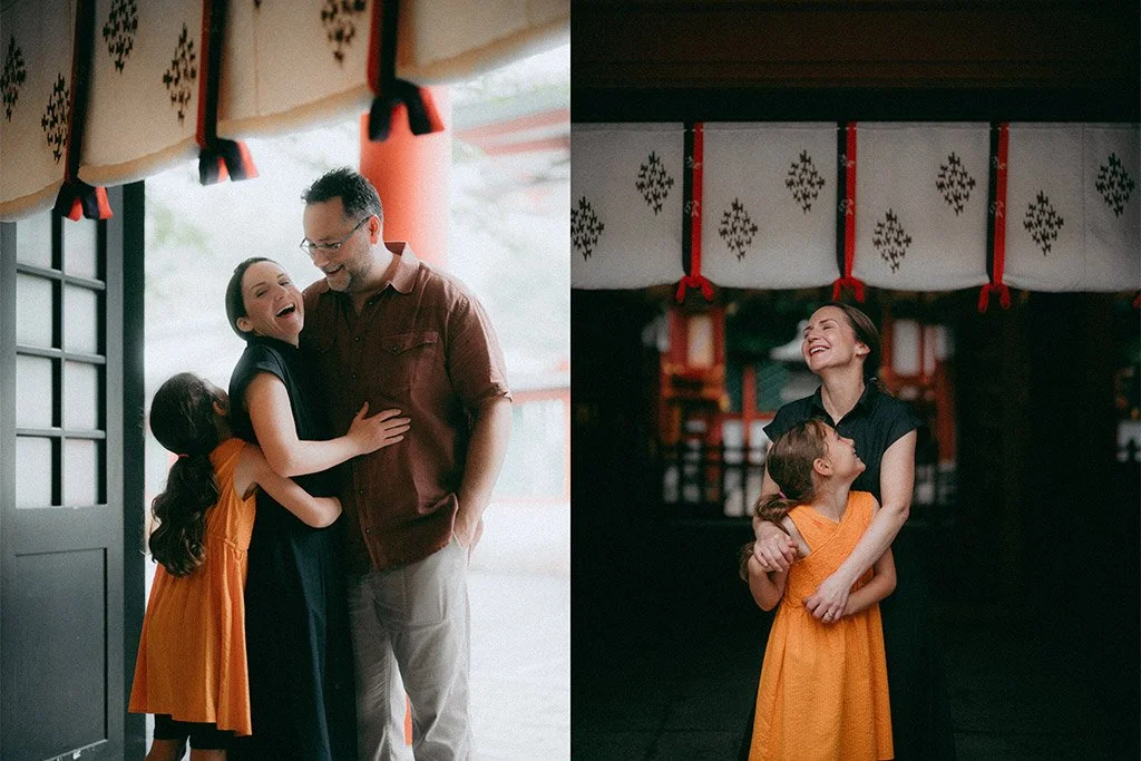 A family of four, including a man, a woman, and two young girls, sharing joyful hugs inside a traditional Japanese building decorated with red and white hanging banners with black symbols.