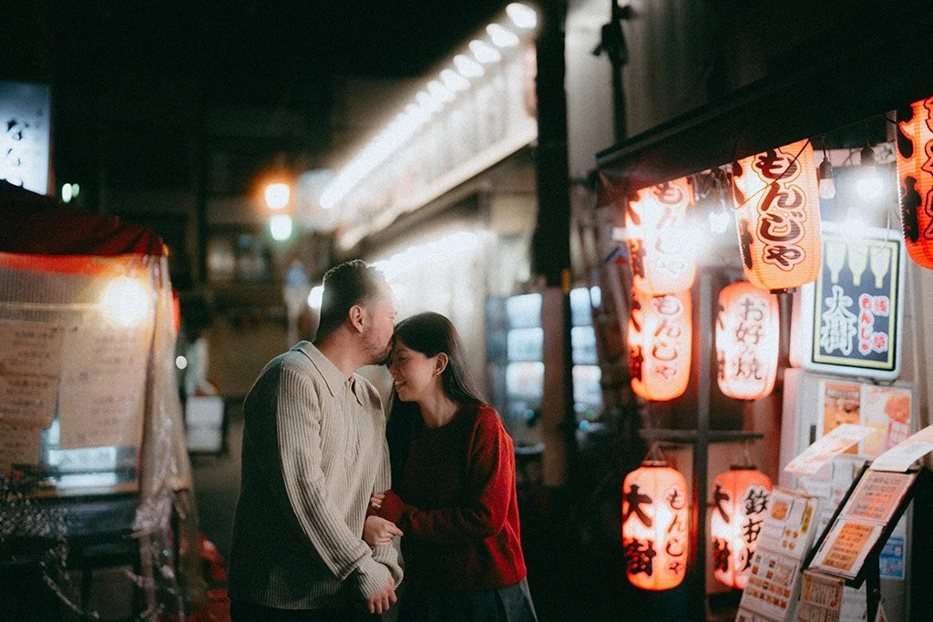 A couple laughing and holding hands outside a Japanese restaurant decorated with red lanterns at night.