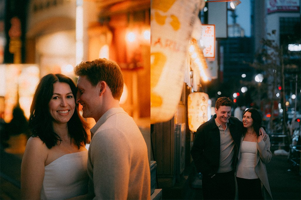 A young couple smiling and walking together at night with lanterns hanging nearby and city lights in the background.