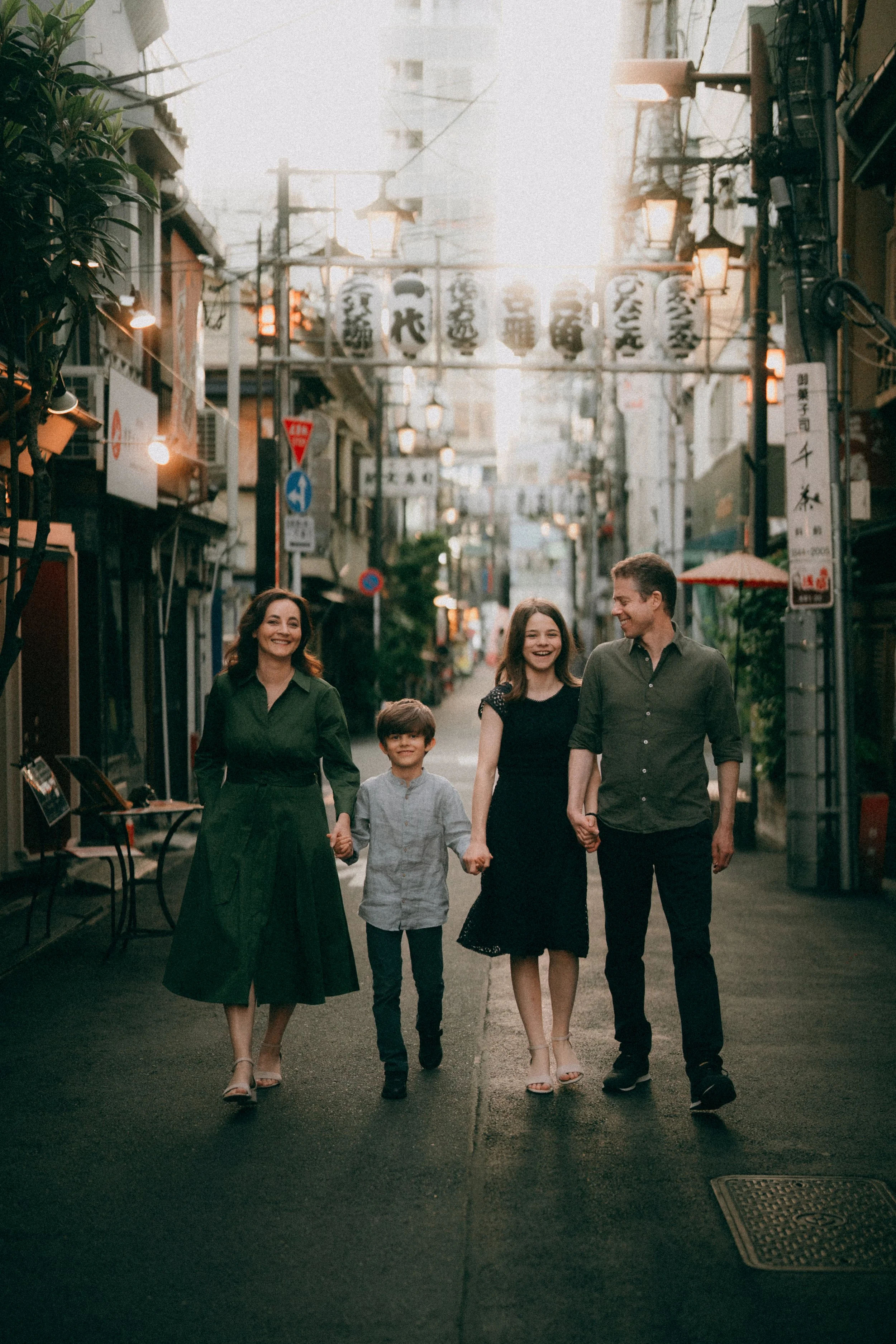A family of four walking hand-in-hand down a city street at dusk, smiling and enjoying each other's company.