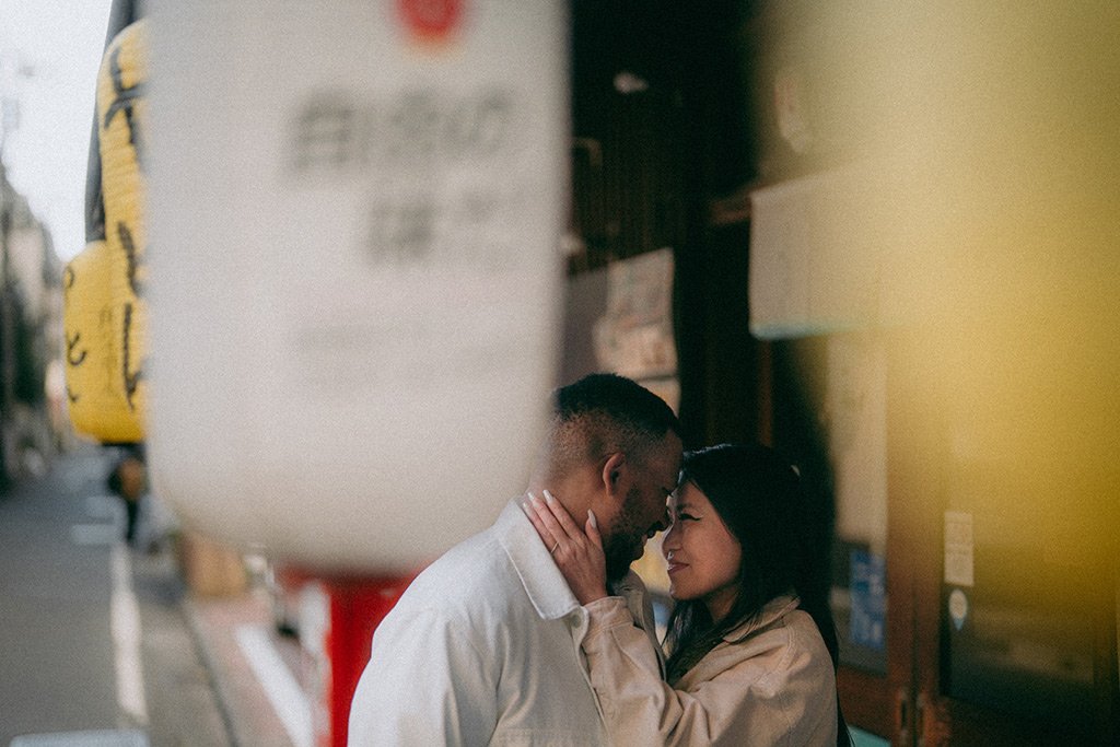 A couple sharing an intimate moment with foreheads touching and smiling gently on a city street at dusk.