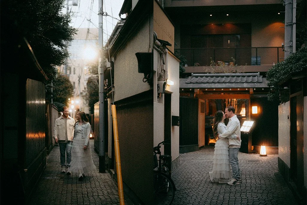 A couple is dancing closely in an entrance area decorated with warm lighting, while a man and woman walk together in a nearby alleyway in the evening.
