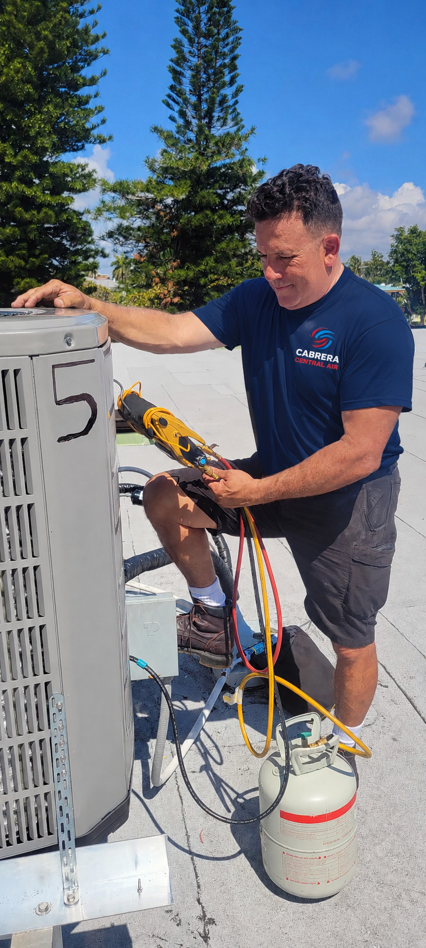 Technician repairing an air conditioning unit on a rooftop, with tools and a canister of refrigerant.