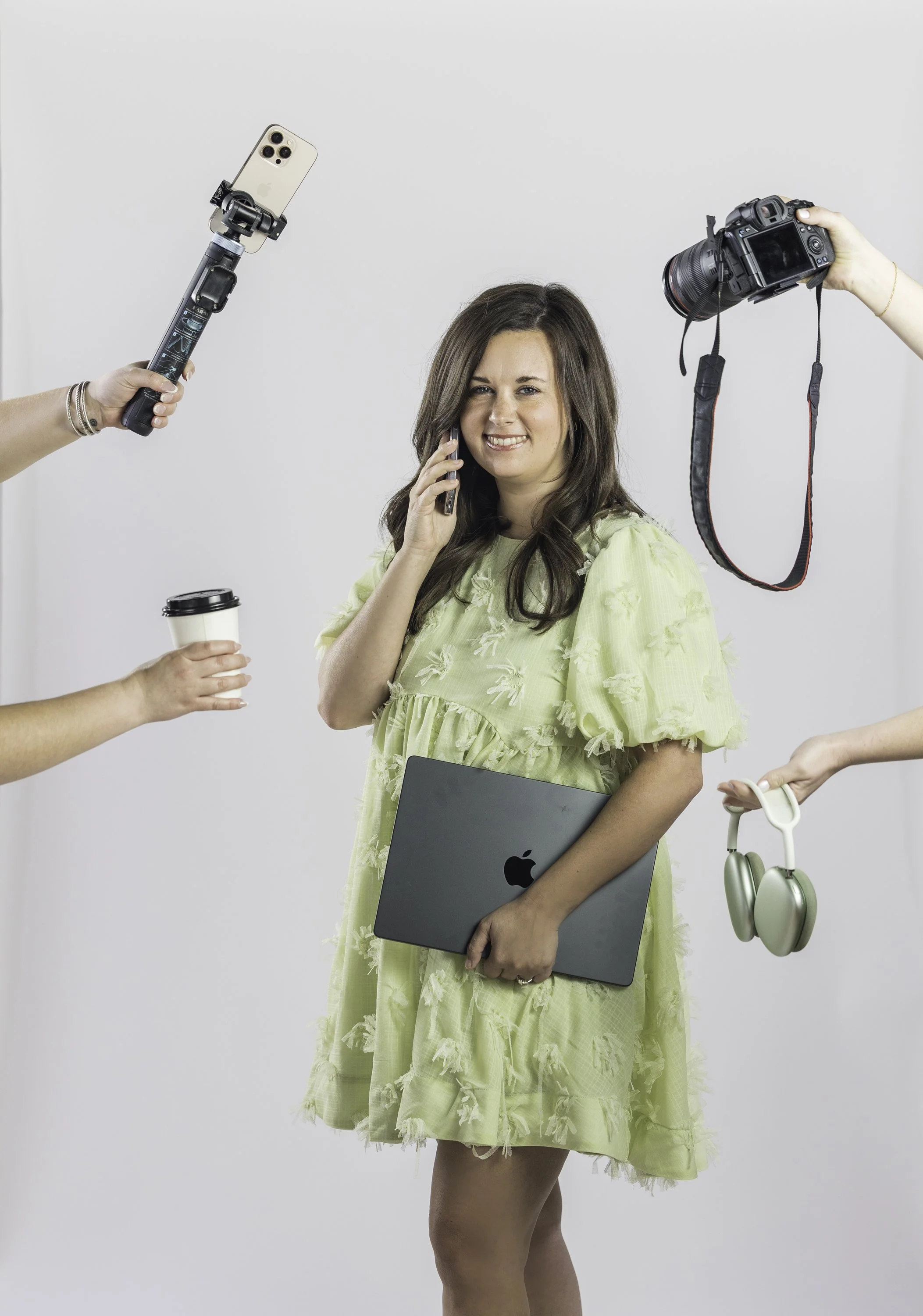 Woman in a yellow dress holding a laptop and talking on a cellphone, surrounded by people taking photos with a camera, a smartphone, a pair of headphones, and a coffee cup.