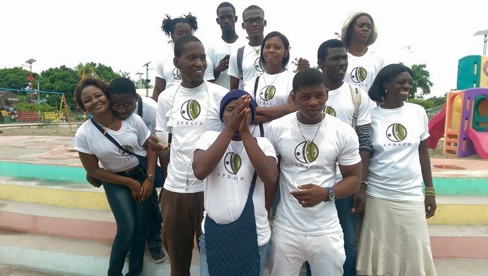 Groupe de personnes portant des T-shirts blancs avec un logo, posant pour une photo à l'extérieur dans une aire de jeux.