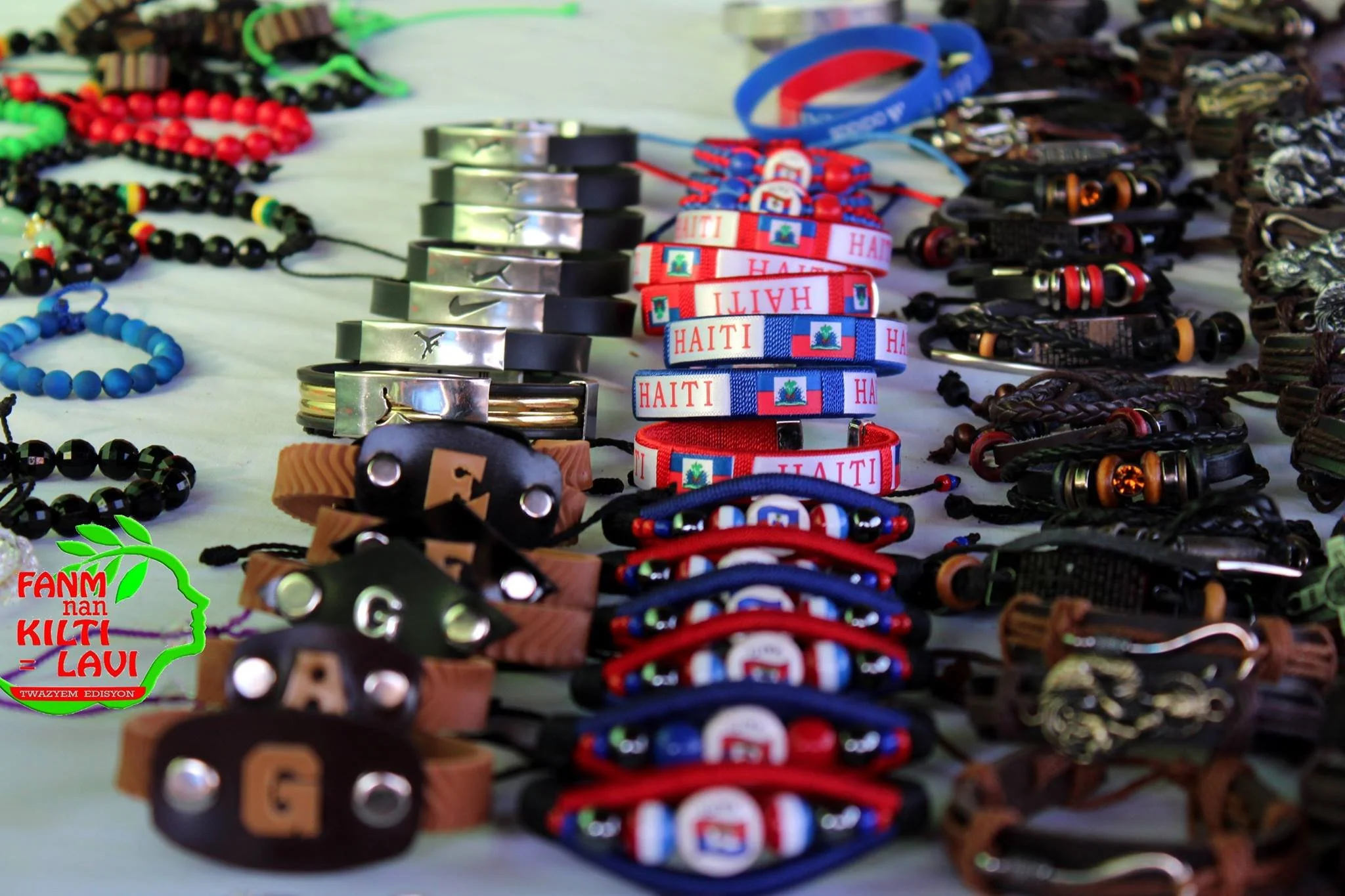 Une présentation de bracelets, de colliers et de bijoux en divers matériaux et couleurs exhibés sur une table, avec des éléments représentant Haïti inclus dans certains raccourcis.