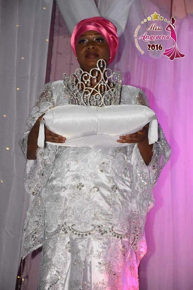 Femme en robe blanche orné de broderies, portant un turban rose, tenant un coussin blanc avec une couronne en perles, à une cérémonie du concours Miss Anacand 2016.