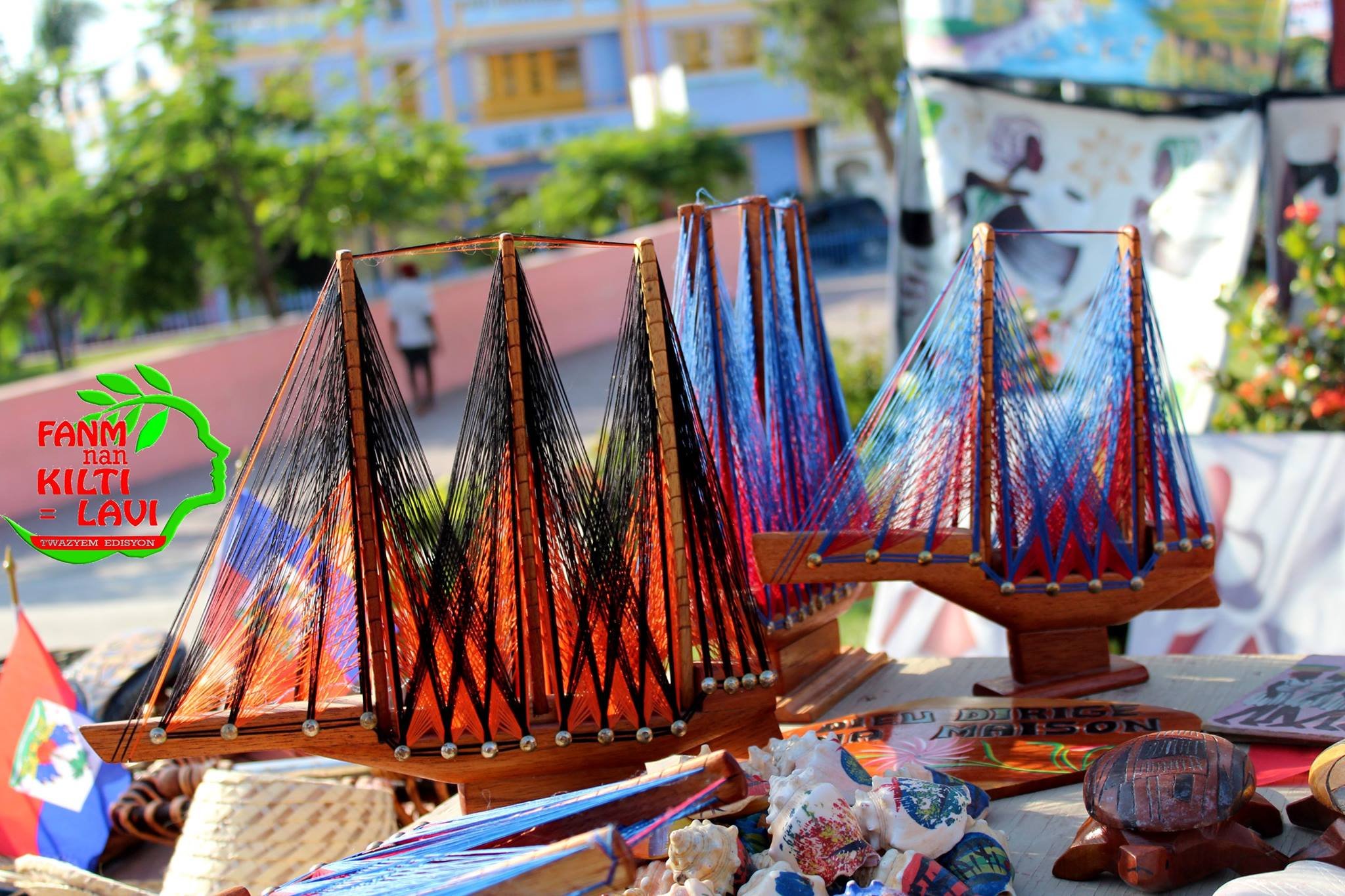 Vente d'objets artisanaux en plein air, incluant des poupées en bois et des objets en coquillage, dans un marché urbain avec des bâtiments en arrière-plan.
