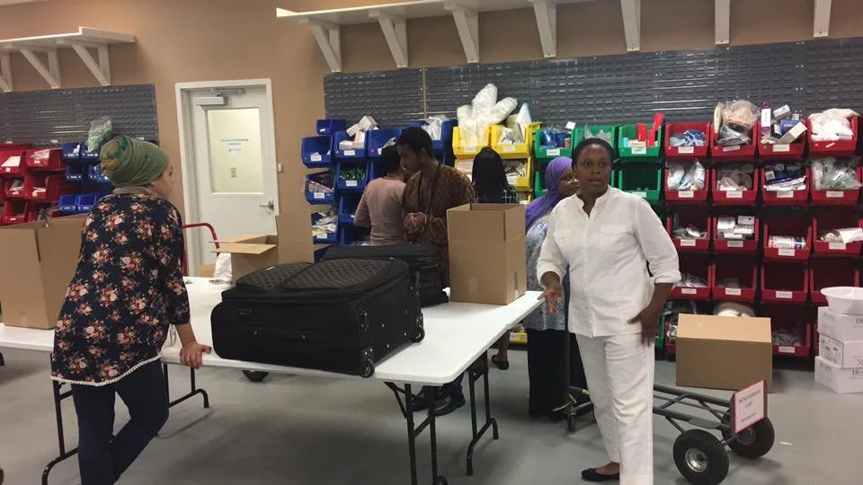 Groupe de personnes en train d'organiser ou de distribuer des fournitures dans une salle de stockage ou un centre de distribution, avec plusieurs caisses et étagères contenant des articles divers.
