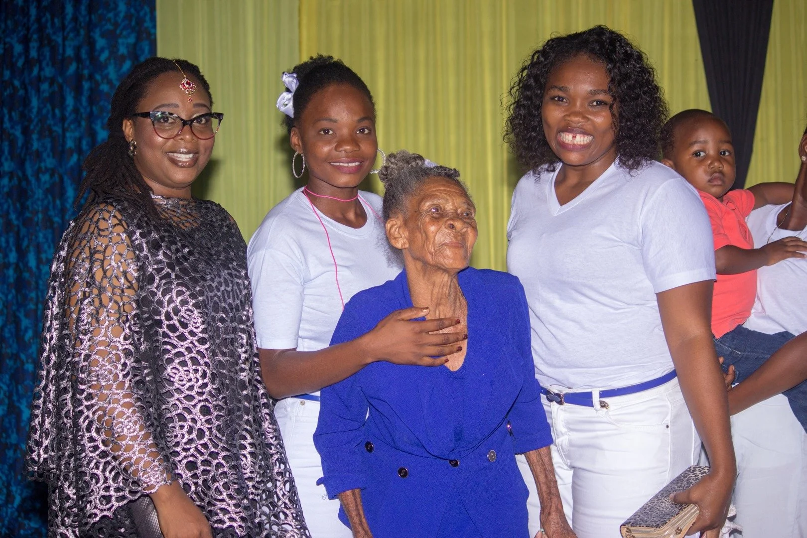 Groupe de femmes et une jeune fille avec une petite fille en arrière-plan, posant pour une photo dans un décor coloré.