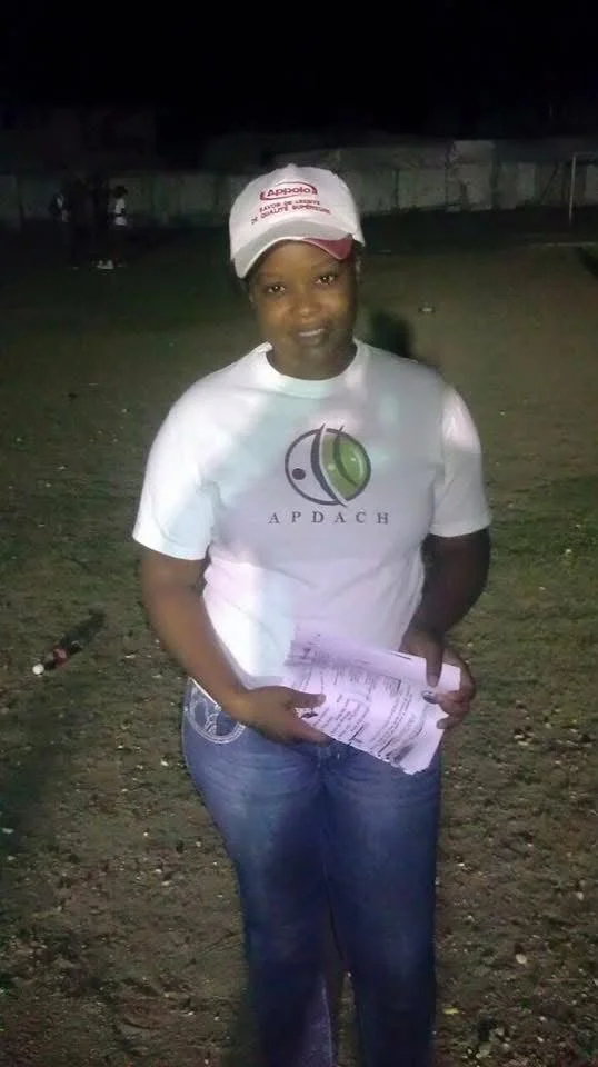 Jeune femme portant un t-shirt blanc avec le logo APDACH, un chapeau blanc avec le logo Apollo, tenant des documents dans un endroit extérieur la nuit.