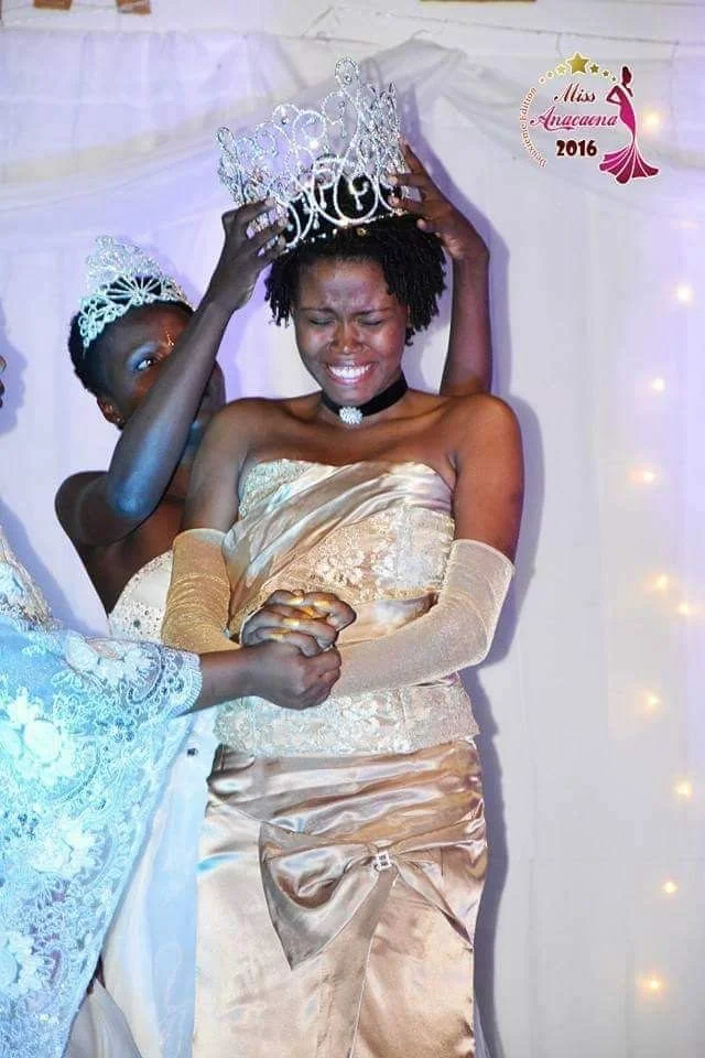 Une jeune femme est en train d'être couronnée lors d'une cérémonie de Miss Anacara 2016, elle sourit avec émotion, portant une robe dorée et un collier noir.