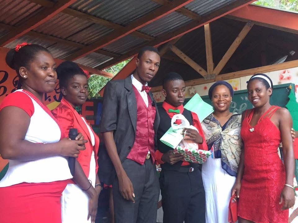 Groupe de six personnes posant pour une photo lors d'un événement célébrant un accomplissement scolaire, portant des tenues formelles et décontractées, dans un espace couvert avec décorations colorées.