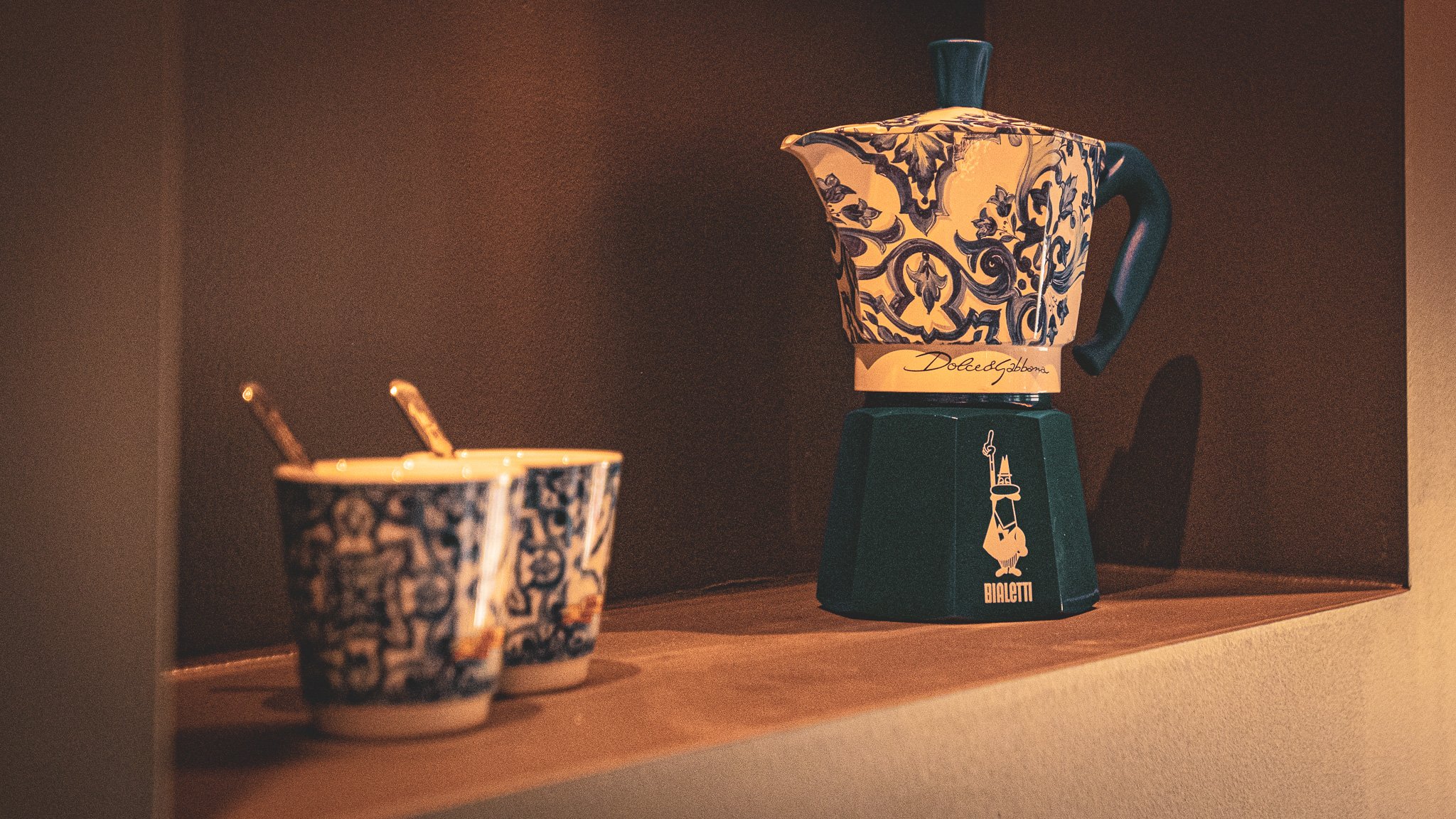 Zwei Tassen mit blumigem Blau-Weiß-Muster und ein blaues Kaffeekessel auf einer Holzablage