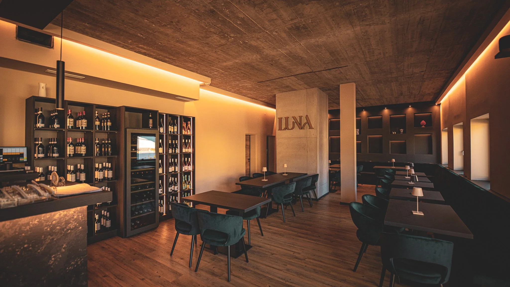 Innenansicht eines modernen Restaurants oder Lounge mit Tischen, Stühlen, Weinregalen und gedämpfter Beleuchtung.