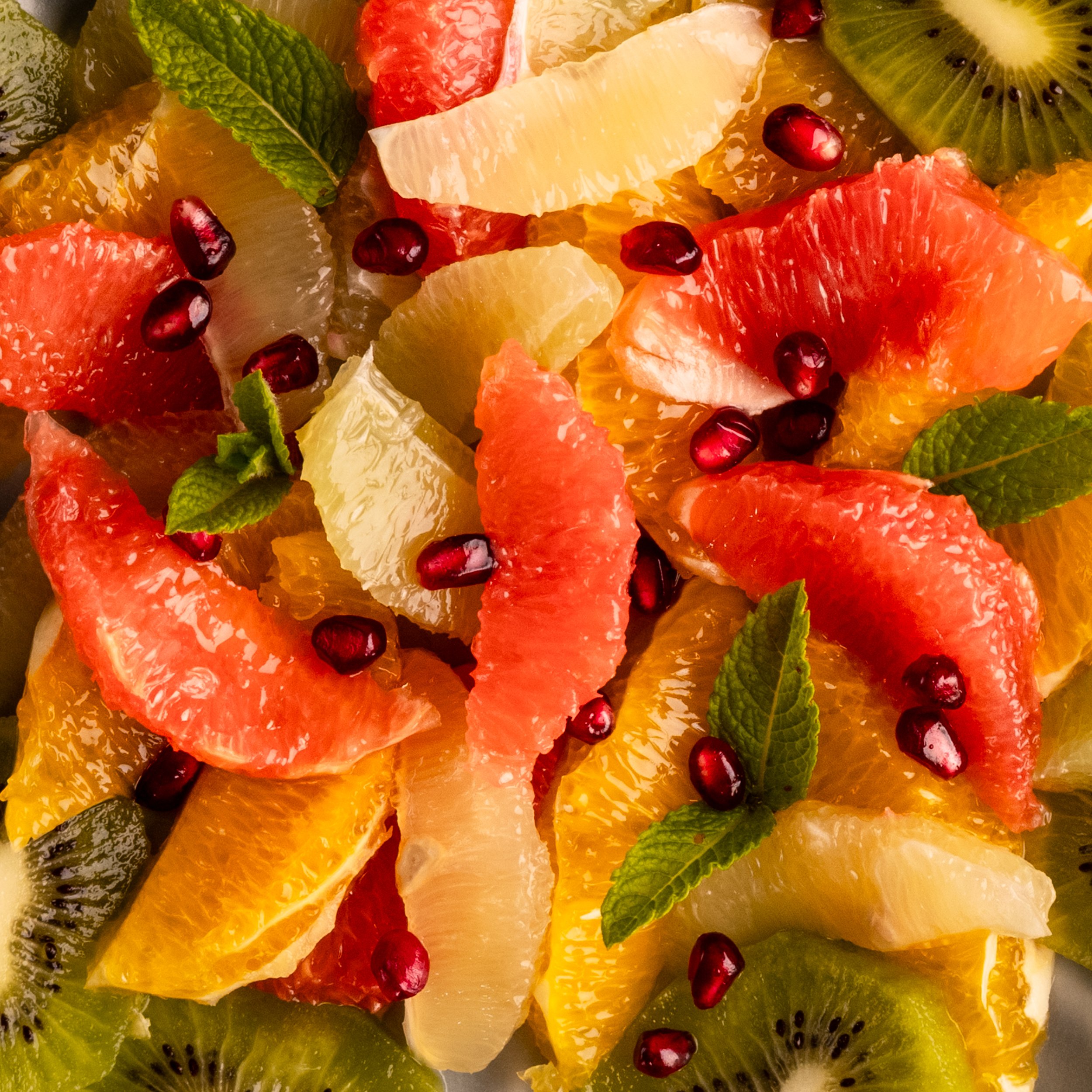 Assorted sliced fruits including kiwi, grapefruit, orange, pomegranate, and lemon, garnished with fresh mint leaves.