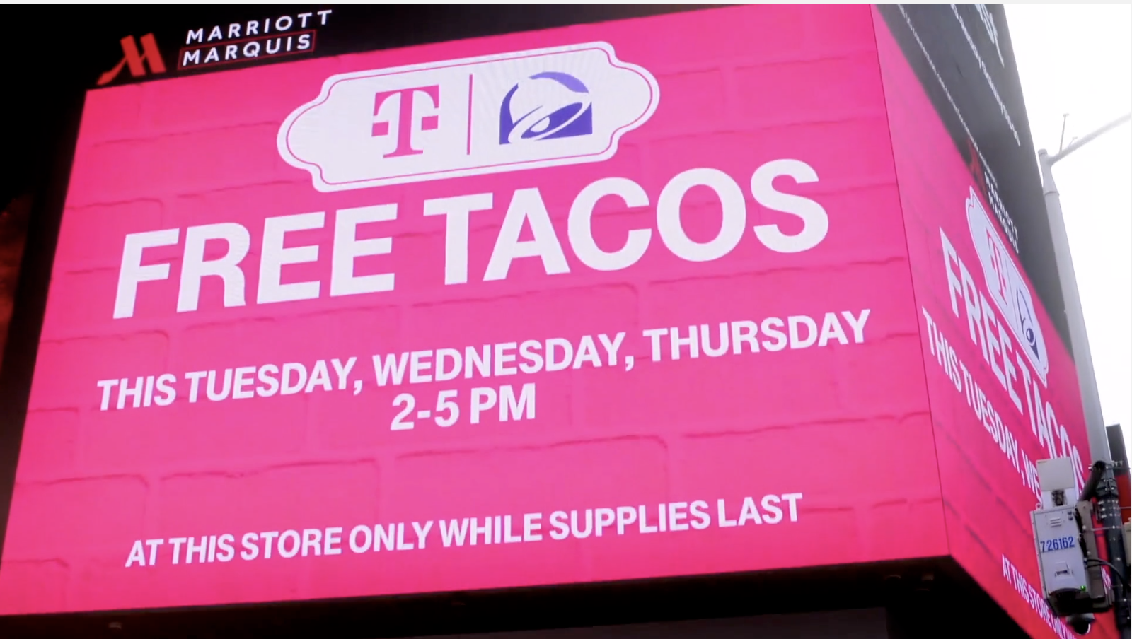 Bright pink billboard advertising free tacos at Marriott Marquis along with Taco Bell and TacoIcon logos, indicating the promotion occurs on Tuesday, Wednesday, and Thursday from 2 to 5 PM, while supplies last.
