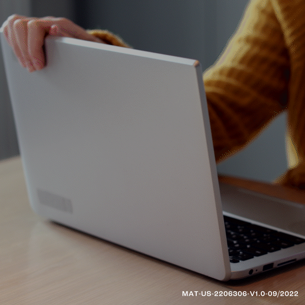 Person in a mustard-colored sweater opening a closed silver laptop on a wooden desk.