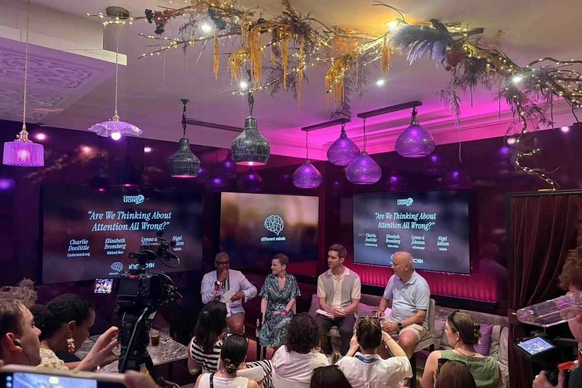 A panel discussion with four speakers seated in front of an audience, with large screens displaying the topic 'Are We Thinking About Attention All Wrong?' and the logos 'Cannes Lions' and 'Different Minds' in a decorated room with purple lighting and hanging pendant lights.
