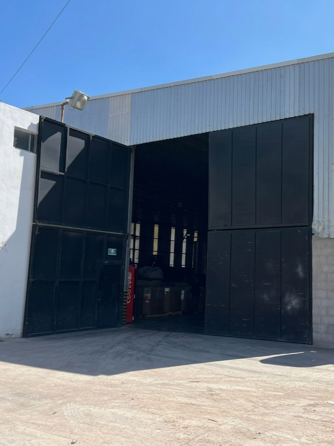 Entrada a un almacén con rejas negras y puerta abierta, visible parte interna con algunos objetos.