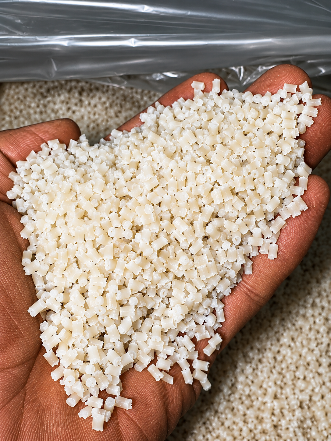 Mano sosteniendo pequeñas piezas blancas de plástico en un entorno de fabricación o procesamiento.