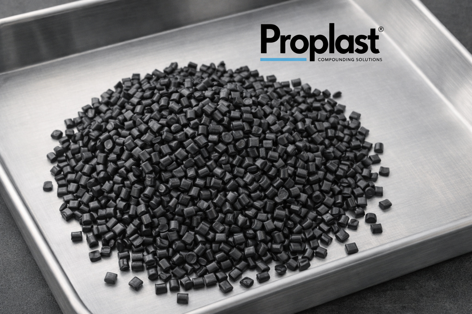 Pequeños pellets negros en una bandeja de acero, con la marca Proplast y el texto 'Soluciones de compuestos' en la esquina superior derecha.