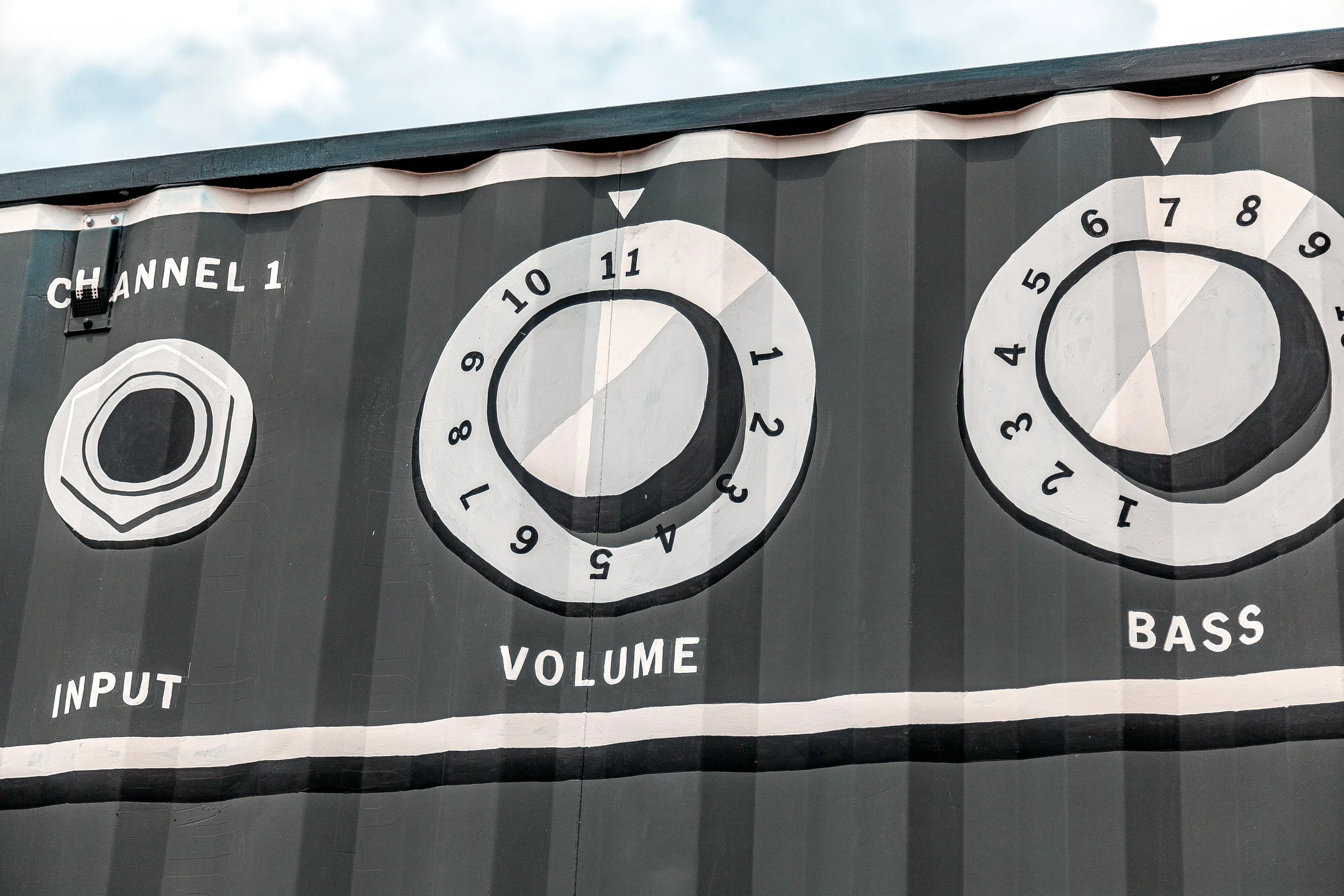 A mural of three large circular knobs representing audio controls with labels for bass, volume, and input on a dark gray background.